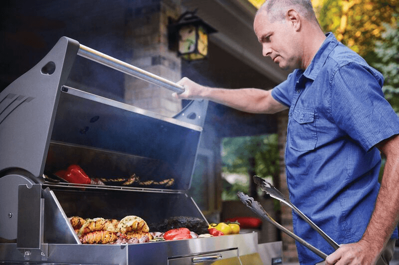 a man cooking on a stainless steel charcoal grill