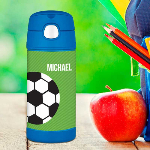Spark & Spark Soccer Fan Green Thermos Bottle with soccer ball design and customizable name 'Michael' on it, placed next to a red apple and school supplies.