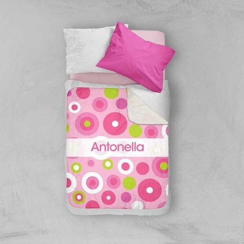 Spark & Spark Circles and Circles Pink Sherpa Blanket, a pink and green circle patterned blanket with personalized name 'Antonella' on it, laid over a neatly made bed with pink and white pillows.
