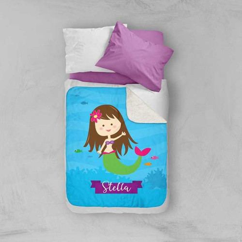 Spark & Spark Cute Mermaid Sherpa Blanket with a personalized design of a girl mermaid named Stella on a blue underwater background, placed on a bed with purple pillows.