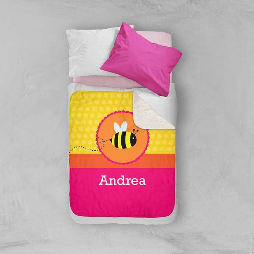Spark & Spark Fly Little Bee Sherpa Blanket, colorful blanket featuring a bee design and personalized with the name Andrea on it, placed on a bed with pink and white pillows.