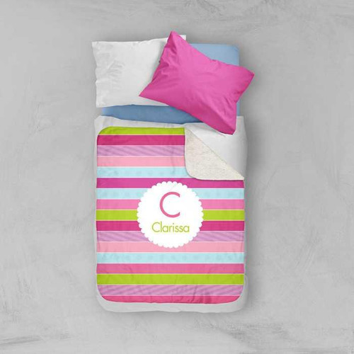 Spark & Spark Pastel Stripes Sherpa Blanket, colorful striped blanket with pink, green, light blue, and white colors, displayed on a bed with pillows.