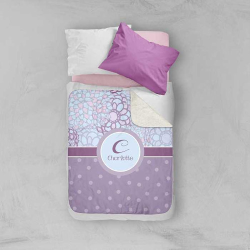 Spark & Spark Flower Mosaic Sherpa Blanket, purple and white floral patterned quilt with personalized name 'Charlotte' on it placed on a bed with pillows.