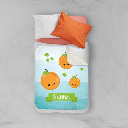 Spark & Spark Yummy Oranges Sherpa Blanket with cute orange fruit characters and the name 'Danna' on the blanket, layered on a bed with pillows.