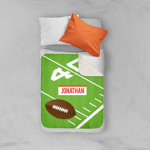 Spark & Spark Football Fan Sherpa Blanket, green and brown football-themed blanket with personalized name 'Jonathan' on a bed with white and orange pillows.