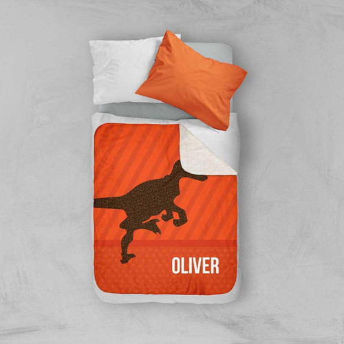 Spark & Spark Dino and Me - Orange Sherpa Blanket, orange blanket with a dinosaur graphic and a personalized name 'OLIVER' on it, placed on a bed with white and orange pillows.