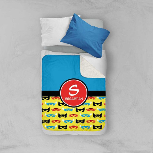 Spark & Spark Super Hero Masks Sherpa Blanket, colorful superhero masks design on the blanket with a personalized name tag, laid on a bed with pillows.