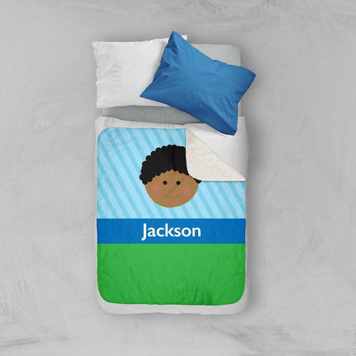 Spark & Spark Just Like Me Boy Lite Blue Sherpa Blanket, a child's bed with a personalized blanket featuring a cartoon boy's face, blue, green, and white colors, and the name Jackson printed on it.