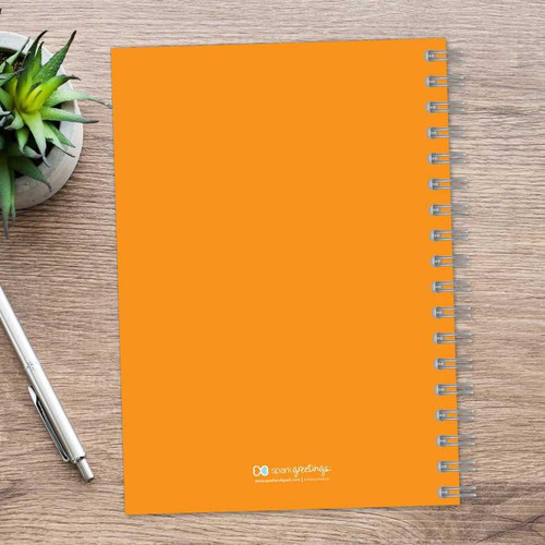SparkGreetings® Simply Dots Writing Journal, orange spiral-bound notebook with dotted pages on a wooden desk with a silver pen and a potted succulent plant