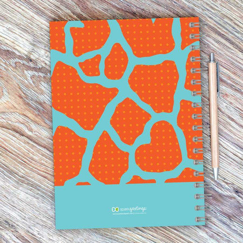 SparkGreetings® Cute Rocks Writing Journal, colorful abstract design with orange and blue pattern on a wooden surface with a pen.
