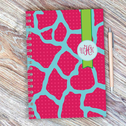 SparkGreetings® Cute Rocks Writing Journal, colorful pink and blue patterned journal with a green ribbon and monogrammed initials, placed on a wooden surface with a matching pen.