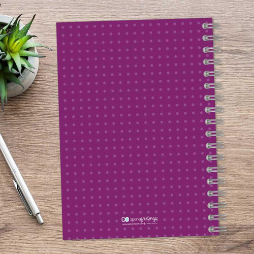 SparkGreetings® Mod Chevrons Writing Journal, purple with a dot pattern, spiral-bound, placed on a wooden surface with a silver pen and a small green succulent plant nearby.