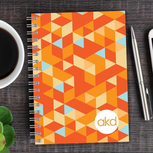 SparkGreetings® Dynamic Ways Writing Journal, colorful geometric pattern notebook with orange, beige, and blue triangles and the 'akd' logo at the bottom right corner.