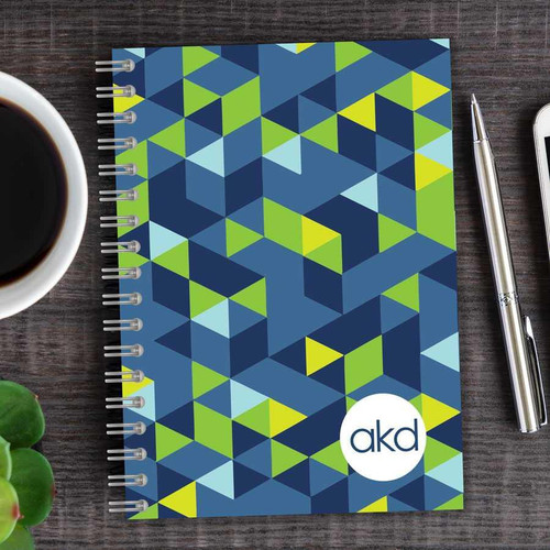SparkGreetings® Dynamic Ways Writing Journal, colorful geometric pattern cover with green, blue, and yellow shapes, spiral-bound notebook placed on a wooden surface.
