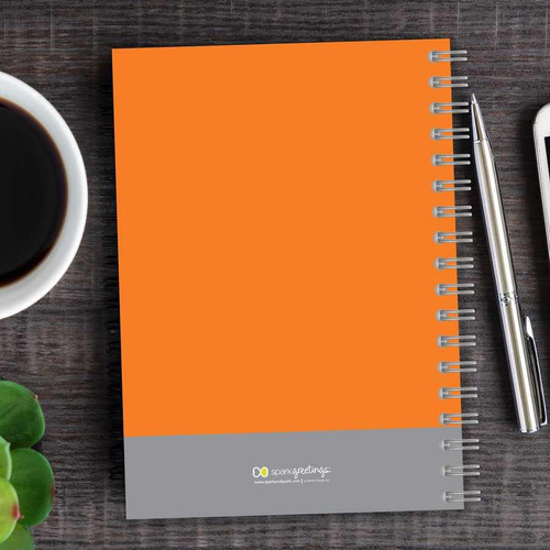 SparkGreetings® Urban Graffitti Writing Journal, orange and grey spiral-bound notebook on a wooden desk with a silver pen and a cup of coffee.