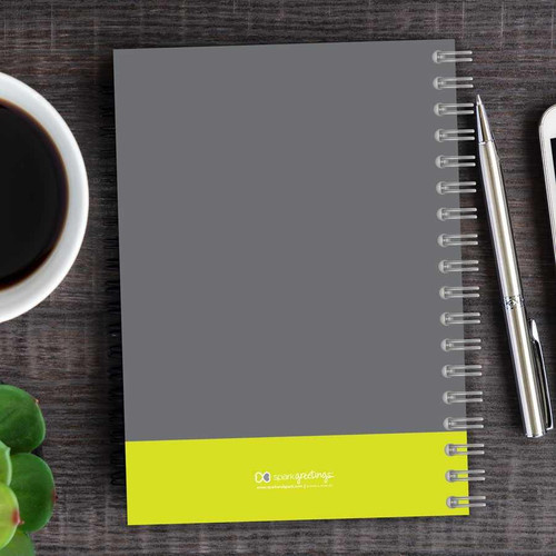 SparkGreetings® Urban Graffiti Writing Journal, front cover with gray and yellow design, spiral binding, placed on a wooden desk with a cup of coffee, a green plant, and a pen.