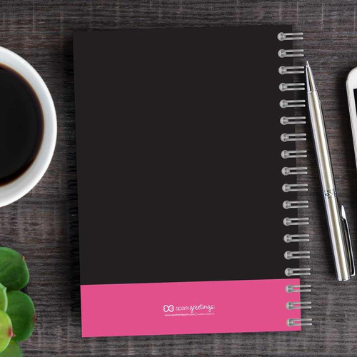 SparkGreetings® Victorian Bold Style Writing Journal, black cover with pink band at the bottom, spiral-bound notebook on wooden desk with pen, coffee cup, and smartphone.