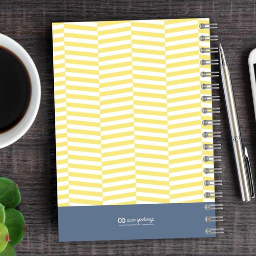 SparkGreetings® Up and Down Style Writing Journal, yellow and white chevron pattern notebook with spiral binding on a wooden desk with a cup of coffee, pen, and smartphone.