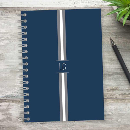 SparkGreetings® Elegant Ribbon Writing Journal, navy blue cover with white and gray ribbon design, spiral-bound notebook on rustic wooden surface with a black pen and green plant.