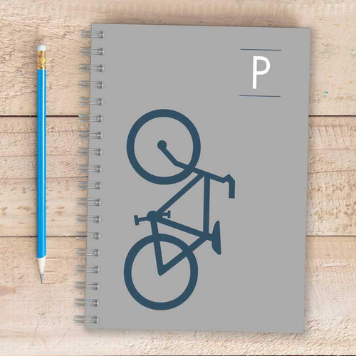 SparkGreetings® Bike Ride Writing Journal, gray spiral-bound journal with a simple bicycle illustration on the cover, placed on a wooden surface alongside a blue pencil.