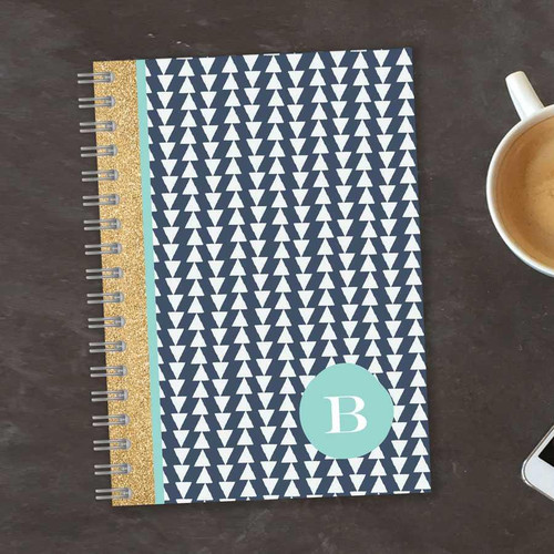 SparkGreetings® Triangles & Glitter Writing Journal, decorated with navy blue and white triangle pattern, gold glitter spine, and a teal monogrammed initial 'B' on the cover.