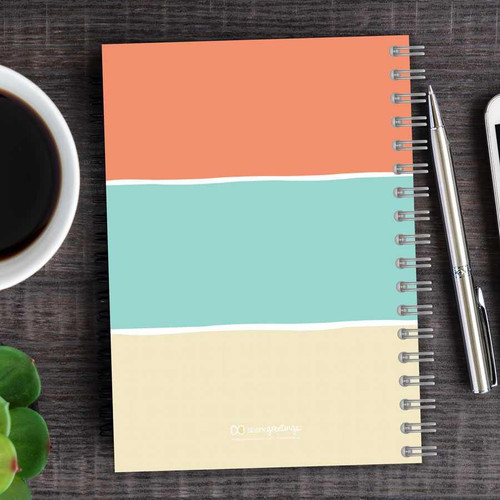 SparkGreetings® Three Stripes Writing Journal, colorful notebook with pastel-colored horizontal stripes on the cover, spiral binding, placed on a dark wooden desk with a coffee cup and pens.