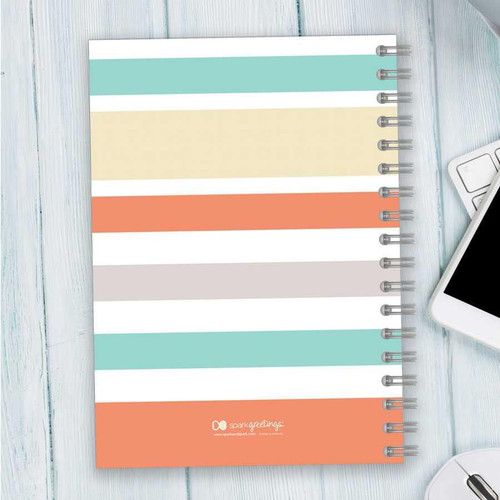 SparkGreetings® Array of Stripes Writing Journal, colorful striped cover design on a spiral-bound notebook placed on a light wooden surface.