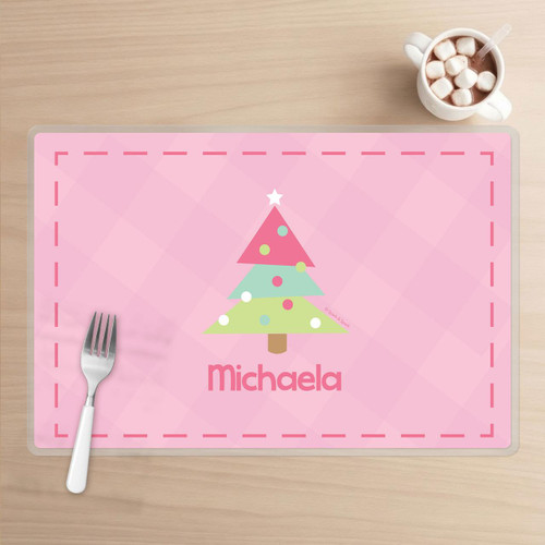 Spark & Spark Modern Xmas Tree - Pink Kids Placemat, pink Christmas tree design with multicolored ornaments and a star on top, personalized with the name 'Michaela' in pink, placed on a light wooden table with a fork and hot chocolate with marshmallows.