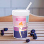 Spark & Spark Cute Gymnast Girl Toddler Cup, a white plastic cup with a lid, straw, and colorful illustration of a young girl gymnast named Elena performing a split on the balance beam, placed on a wooden surface with berries around it.