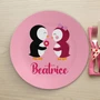 Spark & Spark Penguins in Love Kids Placemat featuring a cute illustration of two penguins, one holding a flower, on a pink background with the name Beatrice written below.