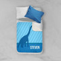 Spark & Spark Dino and Me - Blue Sherpa Blanket, shown on a bed with a white pillow and a blue pillow, featuring a blue dinosaur design and the name 'Steven' on the blanket.