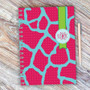 SparkGreetings® Cute Rocks Writing Journal, colorful pink and blue patterned journal with a green ribbon and monogrammed initials, placed on a wooden surface with a matching pen.