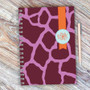 SparkGreetings® Cute Rocks Writing Journal, a spiral-bound notebook with a vibrant purple and pink animal print cover with a round logo and orange ribbon detail.