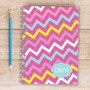 SparkGreetings® Mix Chevrons Writing Journal, colorful chevron pattern with pink, blue, white, and yellow zigzags and dotted accents on a wooden surface.