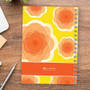 SparkGreetings® Pretty Blooms Writing Journal, a colorful spiral-bound notebook with orange and yellow floral design on the cover placed on a wooden desk.