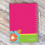 SparkGreetings® Modern Blooms Writing Journal, vibrant pink cover with colorful floral design, spiral binding, and matching pen on wooden surface.