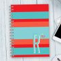 SparkGreetings® Bold and Modern Writing Journal, colorful striped cover with large letter R and personalized name Robyn, on a light wooden surface with part of a laptop and mouse visible.