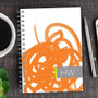 SparkGreetings® Urban Graffiti Writing Journal, spiral-bound notebook with orange graffiti-style cover design on a wooden desk.
