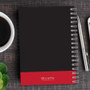 SparkGreetings® Victorian Bold Style Writing Journal, black cover with red bottom band and silver pen on wooden desk with coffee cup and plant.