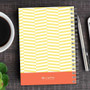 SparkGreetings® Up and Down Style Writing Journal, spiral-bound notebook with yellow and white geometric pattern cover on a wooden desk, next to a silver pen, a cup of coffee, and a smartphone.