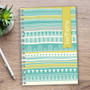 SparkGreetings® Tribal Mood Writing Journal, colorful tribal pattern cover with geometric designs in shades of blue, white, and yellow on a wooden desk.