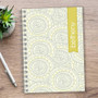 SparkGreetings® Tribal Mood Writing Journal, creative patterned journal with circular tribal motifs in yellow and gray on cover, on wooden desk with a pen and plant nearby.