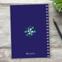 SparkGreetings® Stamped Blossoms Writing Journal, navy blue spiral-bound journal with a colorful floral design on the cover placed on a light wooden surface with a pen and green plant nearby