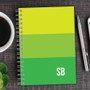 SparkGreetings® Shades of Color Writing Journal, vibrant color-blocked journal with spiral binding, with a cup of coffee and a pen on a wooden surface.