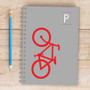 SparkGreetings® Bike Ride Writing Journal, gray spiral notebook featuring a red bike graphic on the cover, placed on a wooden surface with a blue pencil beside it.