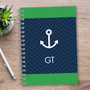 SparkGreetings® Nautical Anchor Writing Journal, navy blue and green cover with anchor graphic and initials GT on a wooden desk with a silver pen and potted succulent plant.