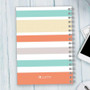 SparkGreetings® Array of Stripes Writing Journal, colorful striped cover design on a spiral-bound notebook placed on a light wooden surface.
