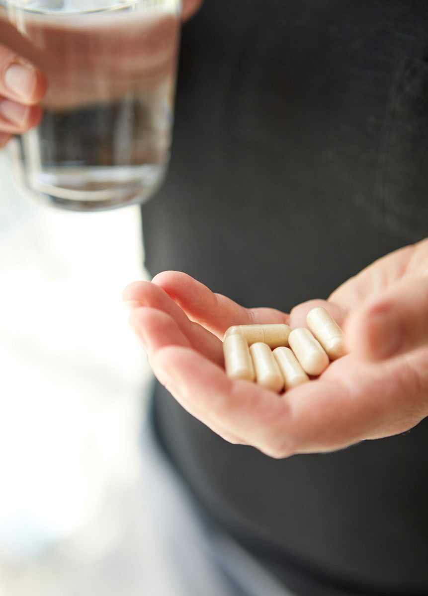 Maca capsules held with a glass of water for daily use