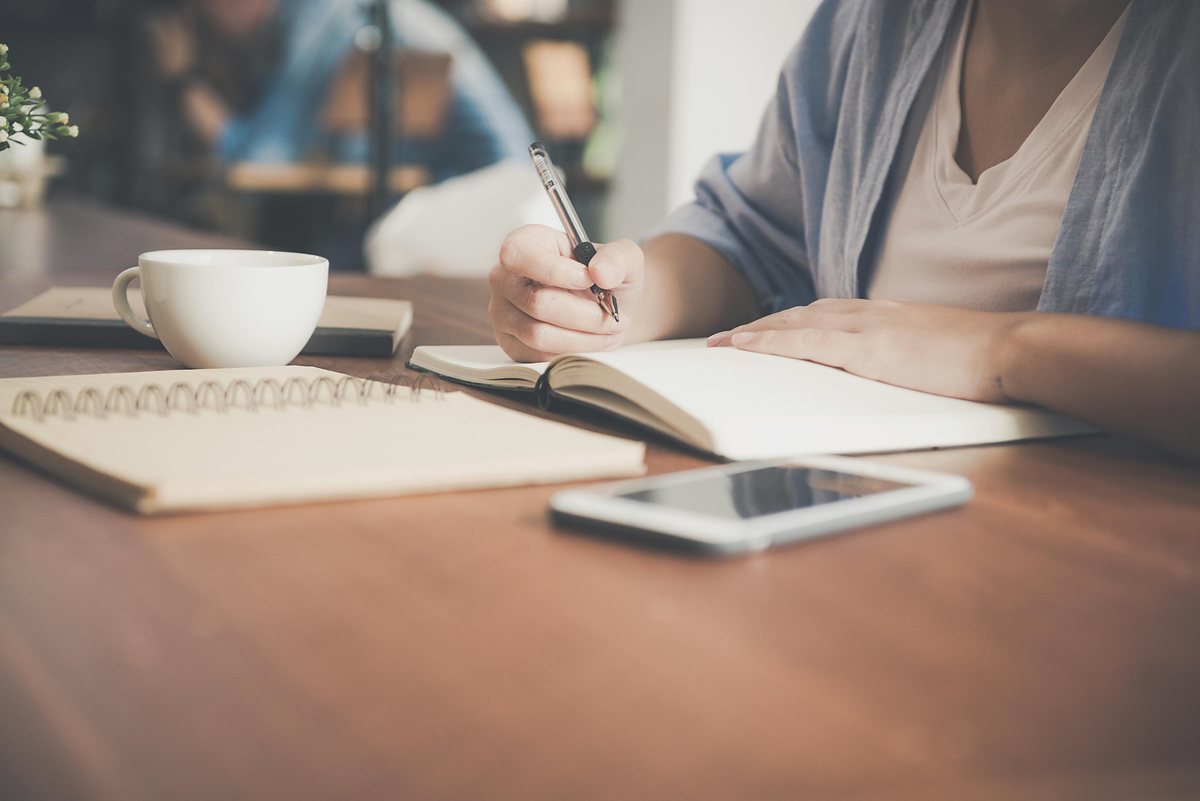 Student writing notes while studying with a cup nearby