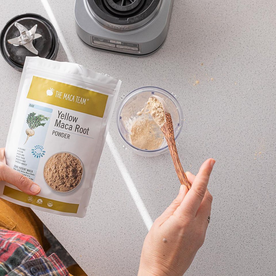 Yellow maca powder being added to a blender cup